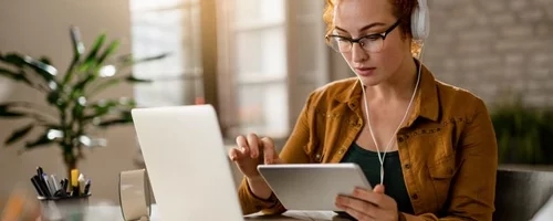 young-creative-businesswoman-working-digital-tablet-while-wearing-headphones-office